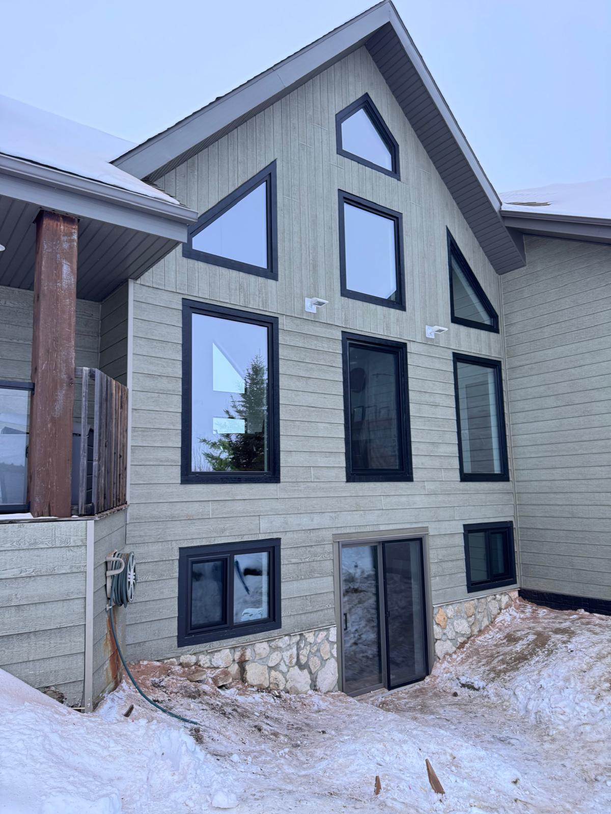 Chalet-style facade with stacked trapezoid and gable black-frame windows on grey siding